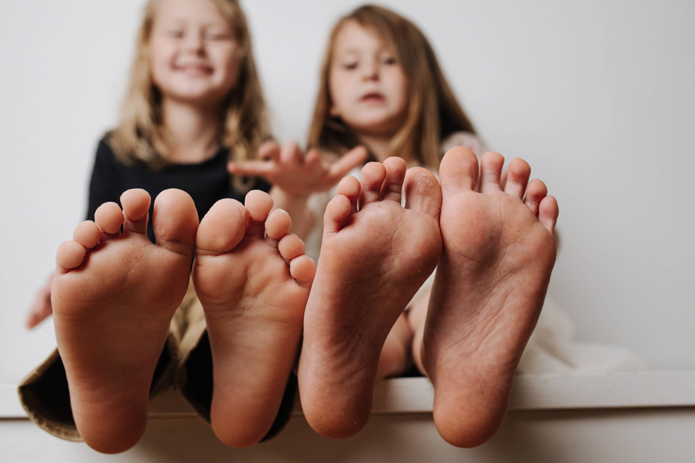 Kids hold feet close up to the camera. Their blurred faces in a background.